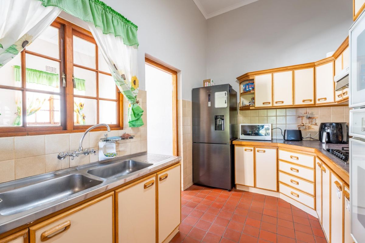 A functional kitchen featuring traditional wooden cabinetry, terracotta floor tiles, a double stainless steel sink, and a tiled splashback.