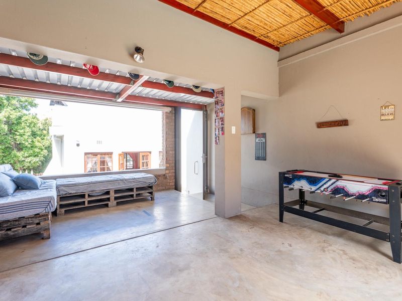 A covered outdoor patio area featuring exposed brick walls, concrete flooring, and a rustic thatched ceiling, providing a versatile space for relaxation or entertainment.