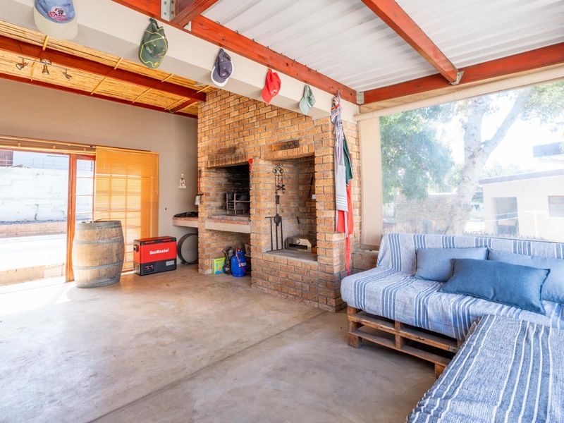 Covered outdoor patio featuring a built-in brick braai, exposed timber beams, and concrete flooring, ideal for relaxed outdoor entertaining.