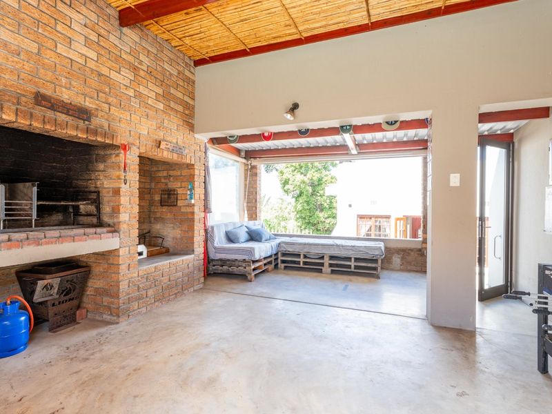 Covered outdoor patio featuring a large built-in brick braai, exposed beam ceiling with bamboo detailing, and concrete flooring, ideal for outdoor entertaining.