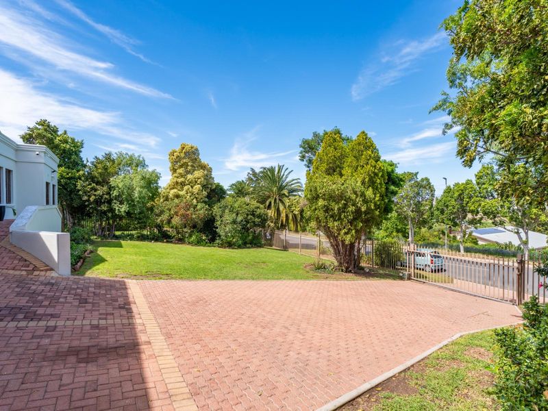 A well-maintained front exterior featuring a spacious brick-paved driveway, landscaped garden area, and secure metal perimeter fencing.