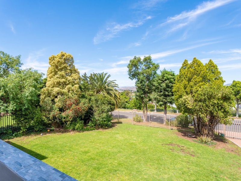 A well-maintained garden area featuring a manicured lawn, mature trees, and secure metal perimeter fencing with a view of the surrounding neighborhood.