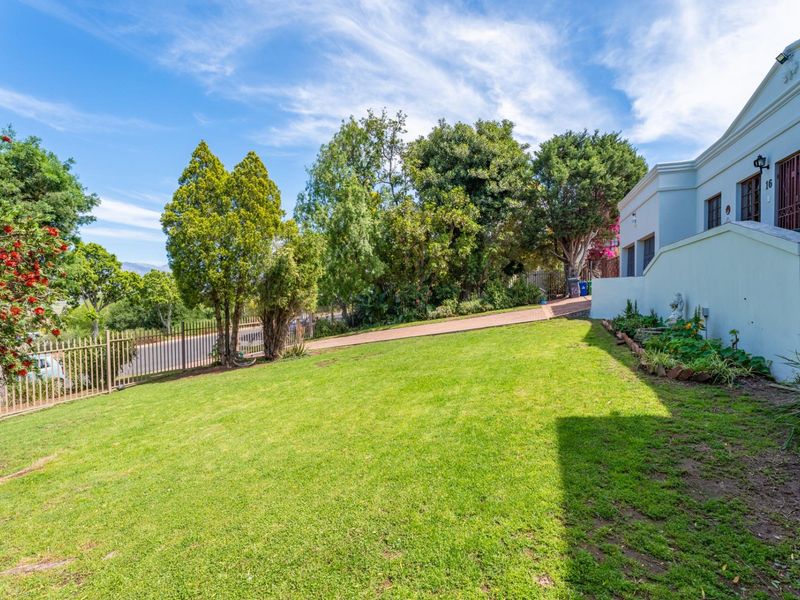 A well-maintained front garden featuring a lush lawn, mature trees, and secure metal perimeter fencing leading to the property entrance.