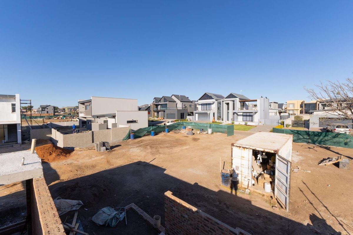 An elevated view of a vacant residential plot under development, surrounded by modern established homes in a developing estate.
