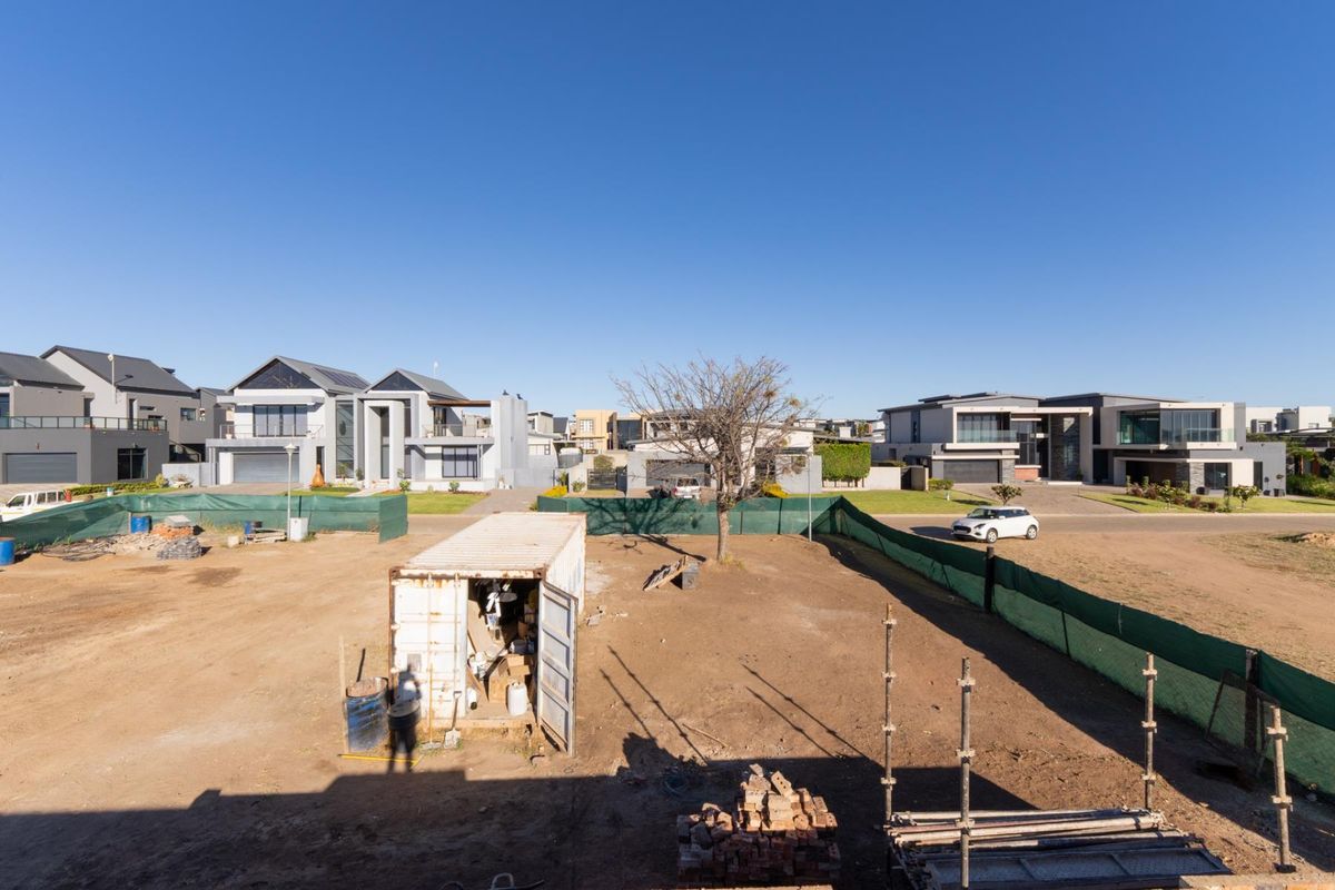 An elevated view of an undeveloped residential plot featuring a temporary storage container and construction materials, situated within a developed suburban estate.
