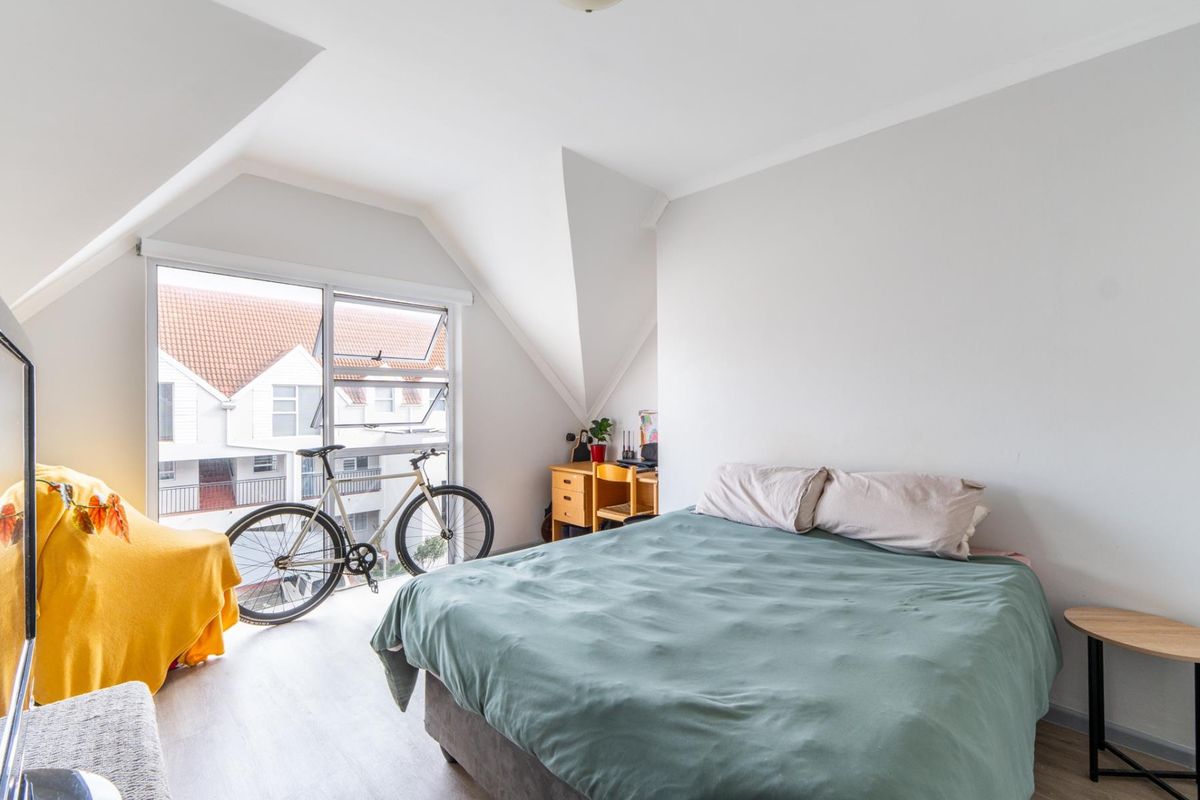 A bright bedroom featuring vaulted ceilings, light-toned flooring, and large windows that provide ample natural light and a view of the surrounding complex.