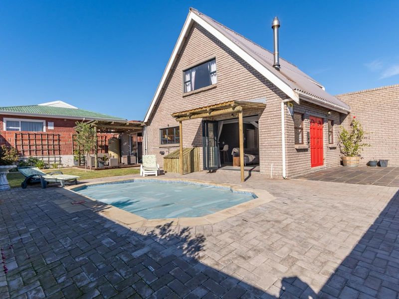 Rear exterior view featuring a paved patio area, a swimming pool with a cover, and a brick-built house with a timber pergola.