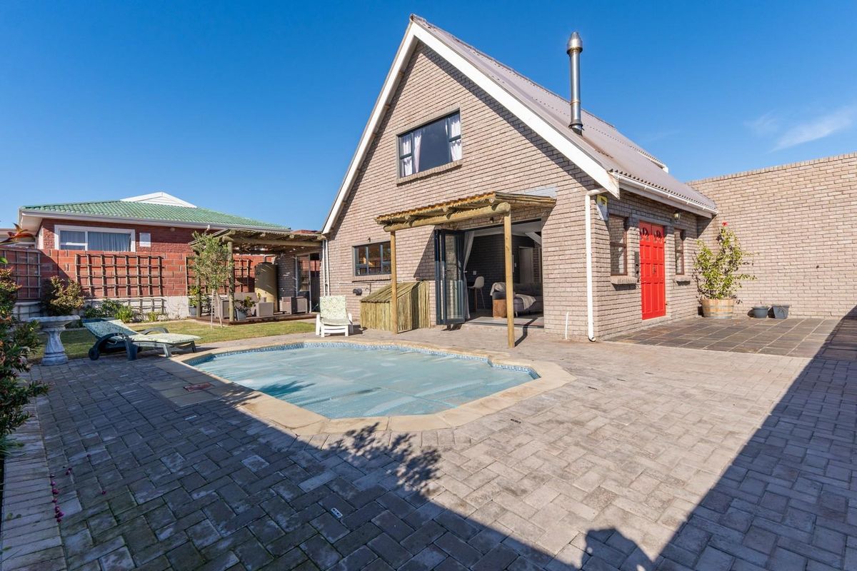 Rear exterior view featuring a paved patio area, a swimming pool with a cover, and a brick-built house with a timber pergola.