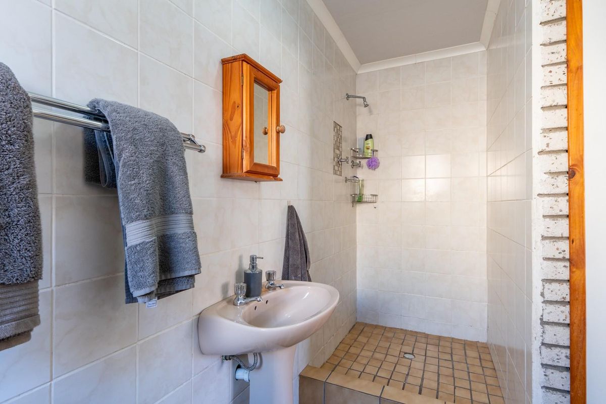 A functional bathroom featuring a pedestal basin, walk-in shower area, and neutral wall tiling throughout.