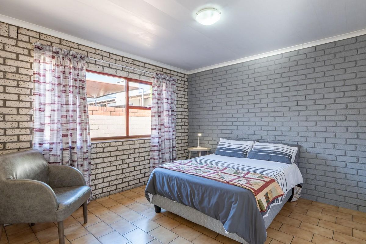 A bedroom featuring exposed brick walls, tiled flooring, and a built-in wardrobe, offering a functional and well-maintained living space.