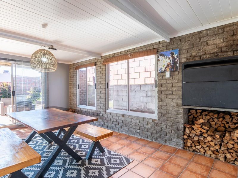 A covered patio area featuring a built-in fireplace, exposed brick walls, tiled flooring, and sliding glass doors leading to the garden.