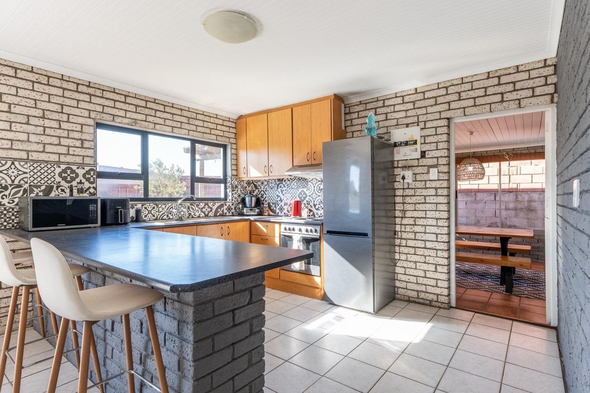 A functional kitchen featuring a breakfast bar, brick wall accents, patterned backsplash tiles, and built-in cabinetry with an integrated oven and hob.