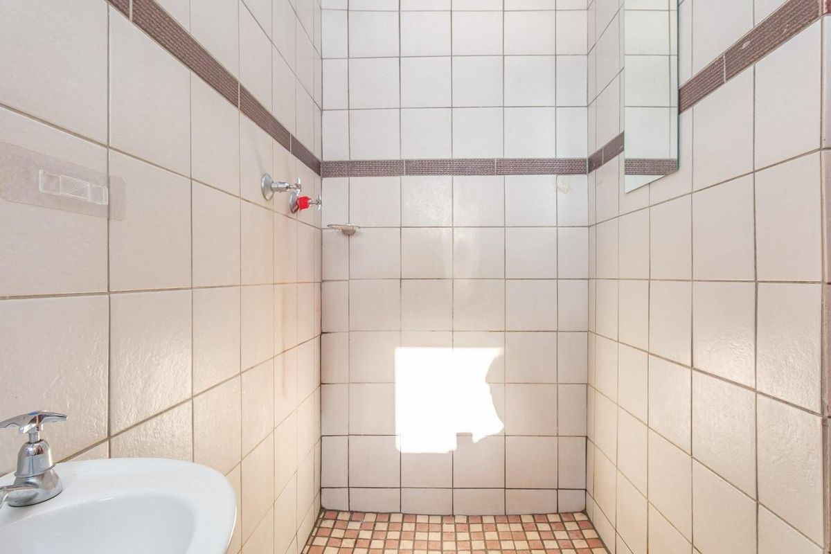A compact bathroom featuring tiled walls and flooring, a wall-mounted basin, and a shower area with basic fixtures.