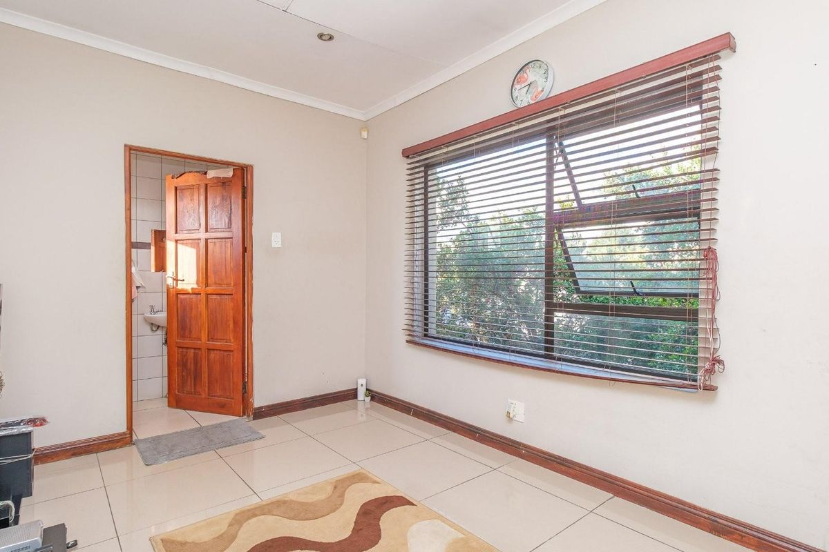 A bright bedroom featuring large windows with fitted blinds, tiled flooring, and direct access to an en-suite bathroom with a wooden door.