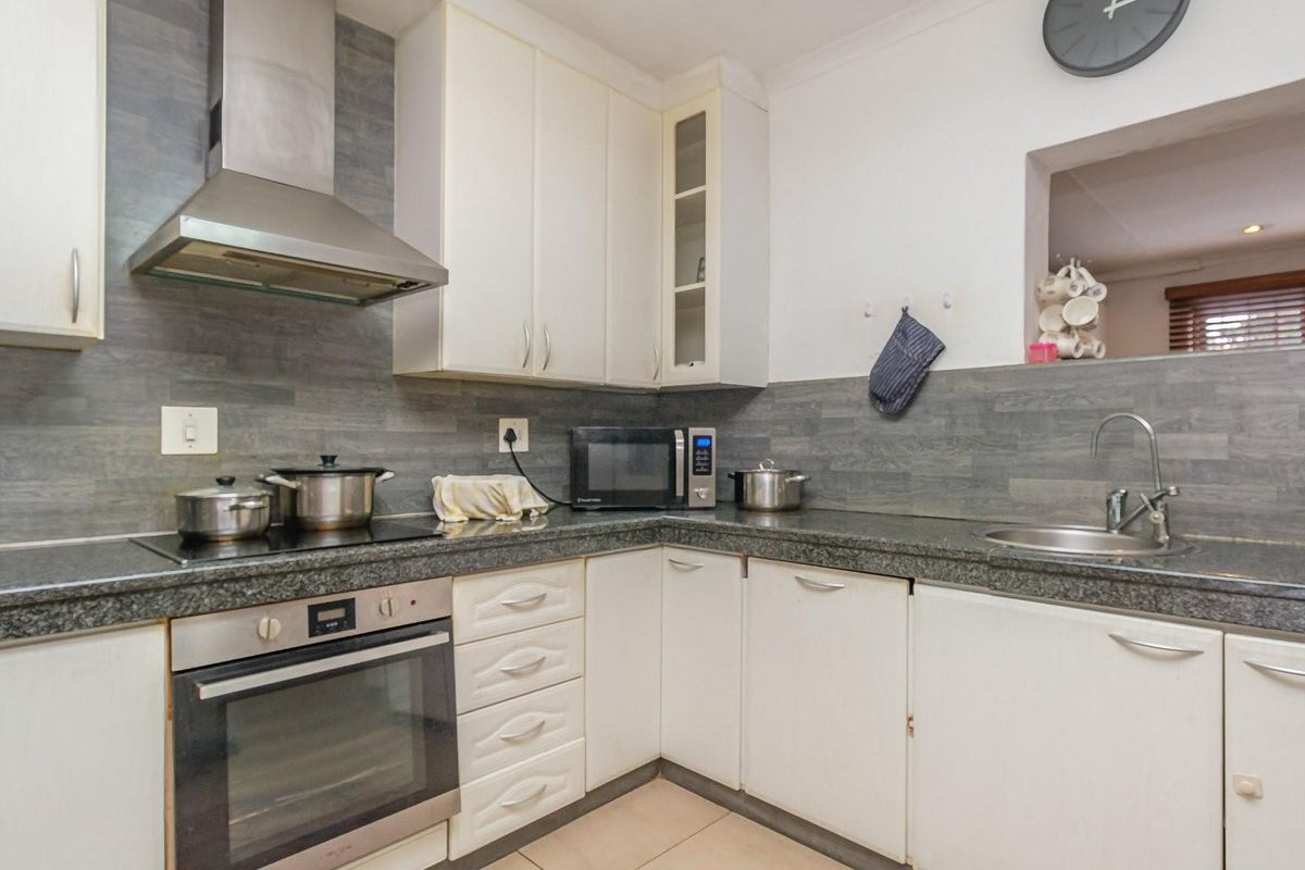 A functional kitchen featuring white cabinetry, granite-style countertops, a built-in oven, glass cooktop, and a stainless steel extractor fan with grey tiled splashbacks.