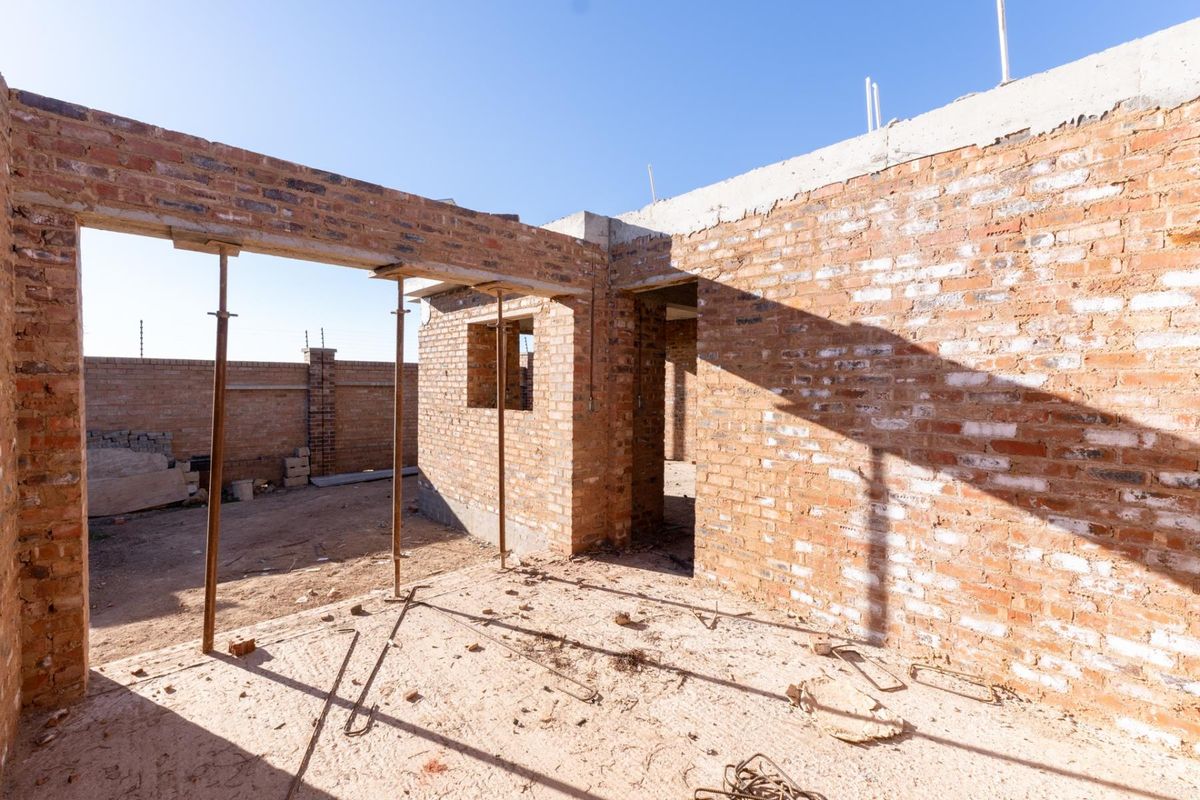 An unfinished residential construction site showing exposed brick walls, structural openings, and temporary support props in a developing property.