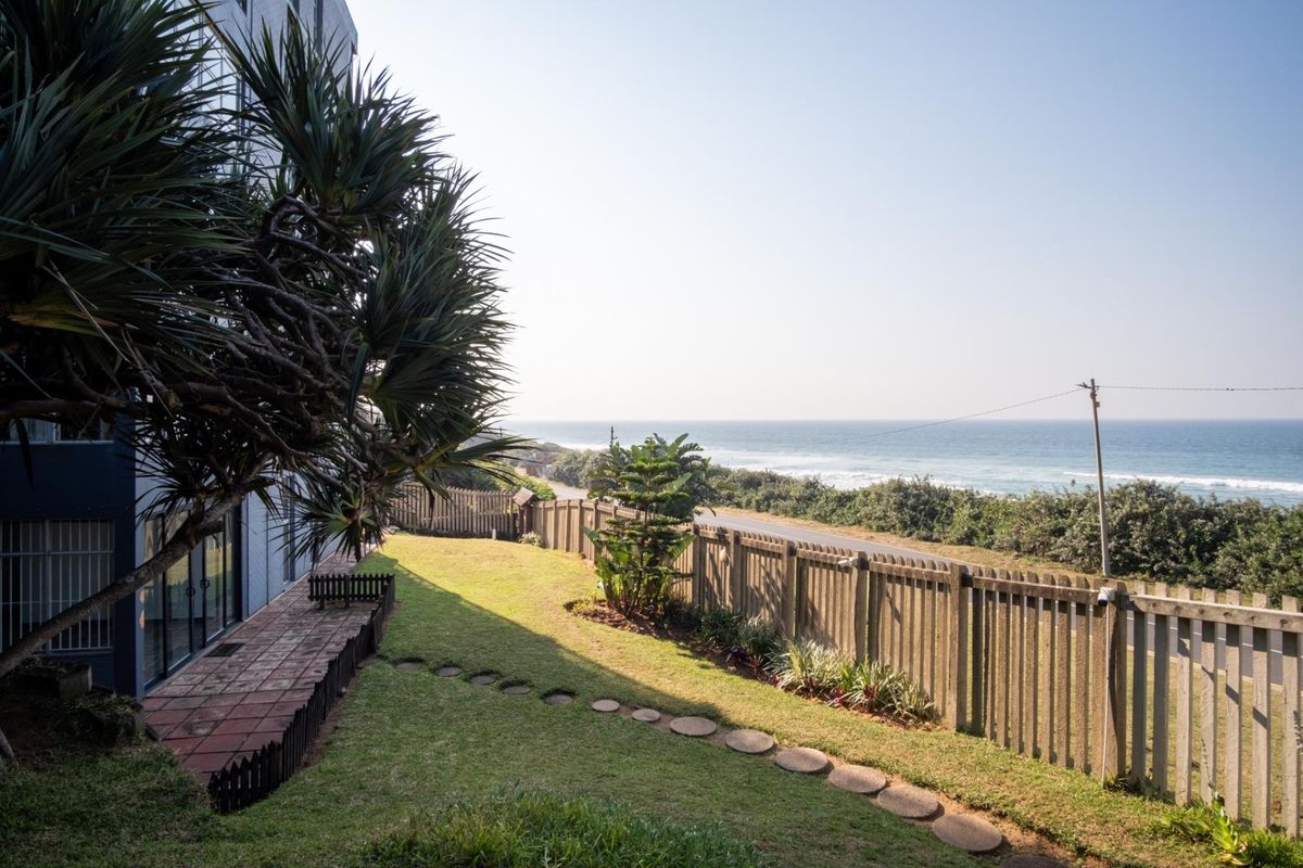 Rear garden area featuring a paved patio, lawn, stepping stone path, and timber fencing with direct views of the nearby coastline.