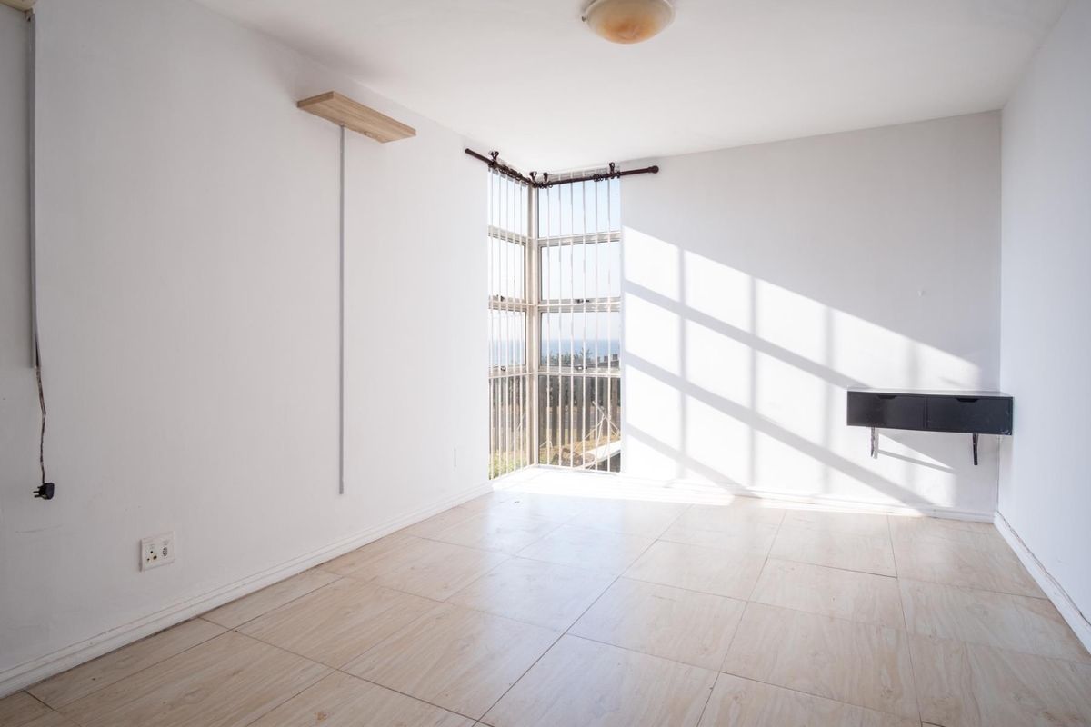 A bright, empty bedroom featuring tiled flooring, a corner window with security bars, and neutral white walls, offering a blank canvas for personalization.
