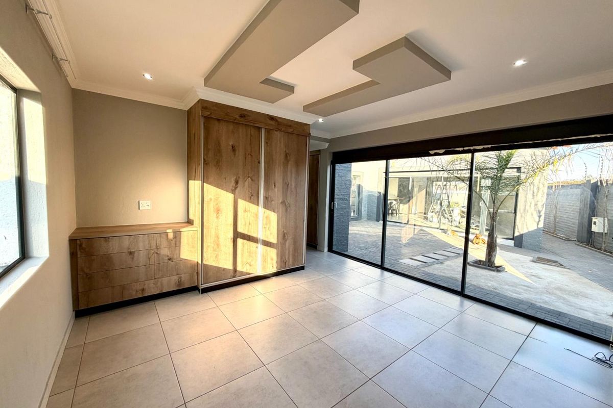 A bright bedroom featuring built-in wooden cabinetry, tiled flooring, a modern recessed ceiling design, and large sliding glass doors opening to the rear patio.