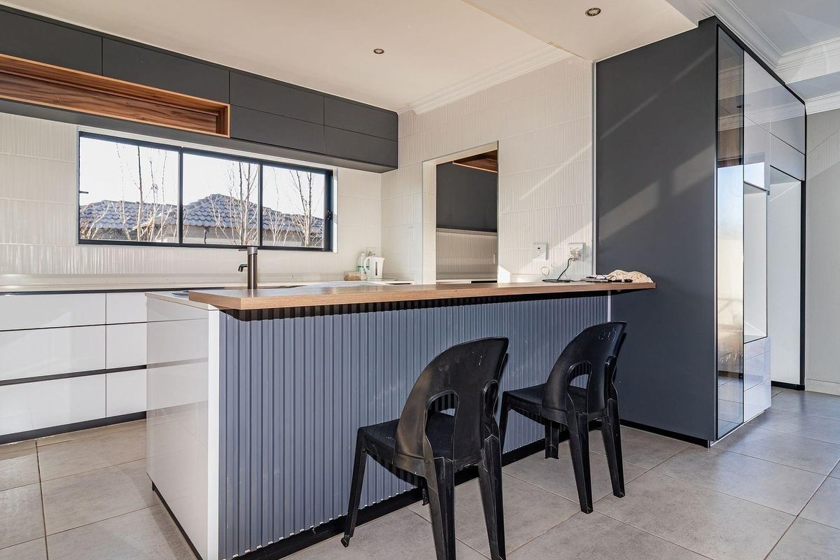 Modern kitchen featuring a central island with breakfast bar, sleek cabinetry, tiled splashbacks, and large windows providing ample natural light.