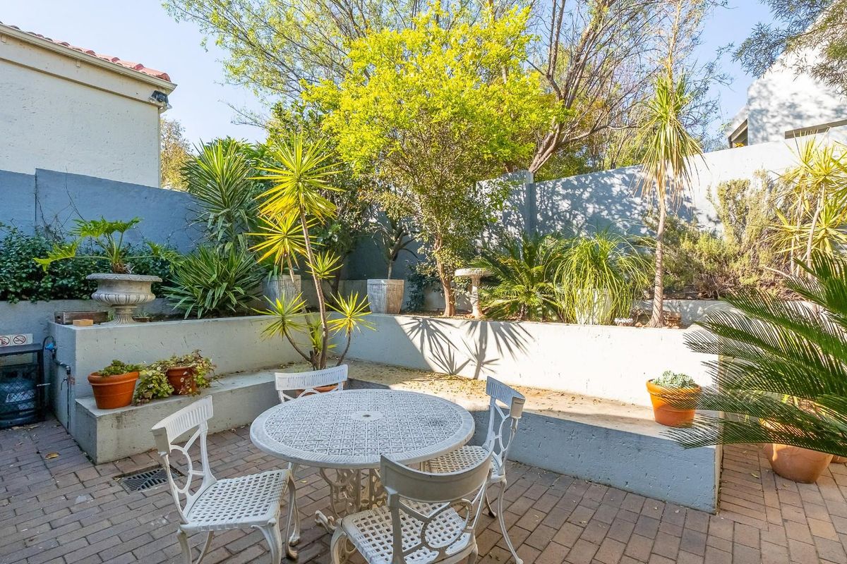 A private rear garden featuring a paved patio area, tiered concrete retaining walls, and established landscaping.