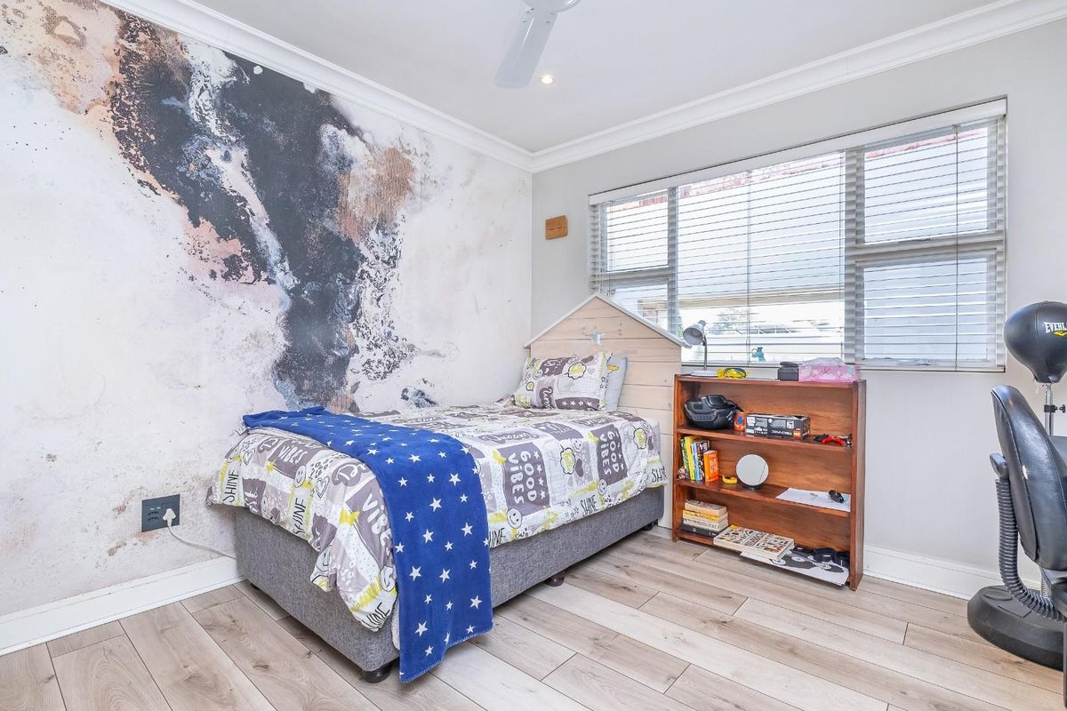 A well-maintained bedroom featuring light wood-look flooring, a decorative feature wall, and a ceiling fan.