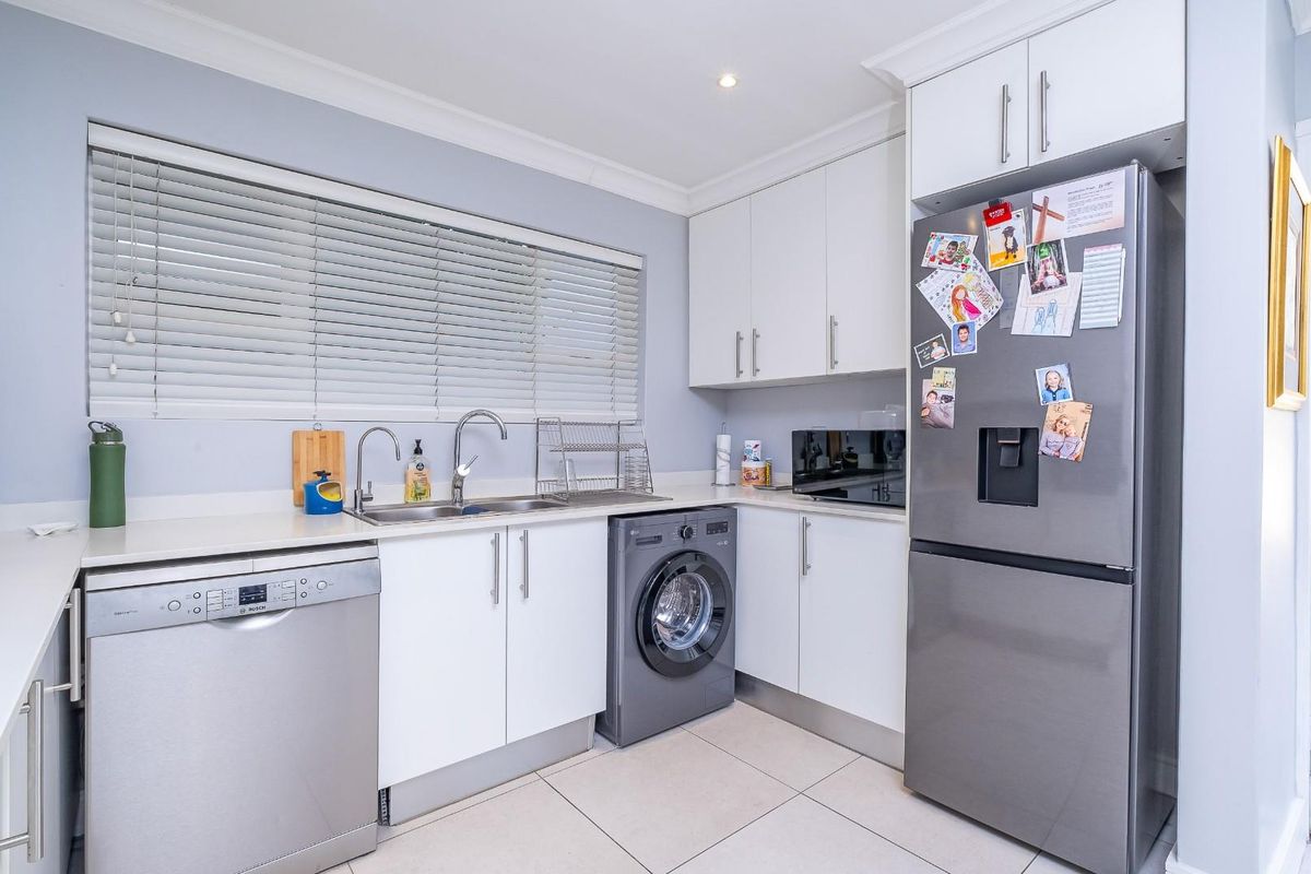A functional kitchen and laundry area featuring white cabinetry, stone countertops, a double sink, and integrated space for a dishwasher and washing machine.