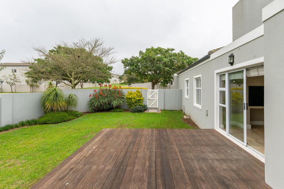 A private rear garden featuring a timber deck, manicured lawn, perimeter boundary wall, and sliding glass door access to the interior living space.