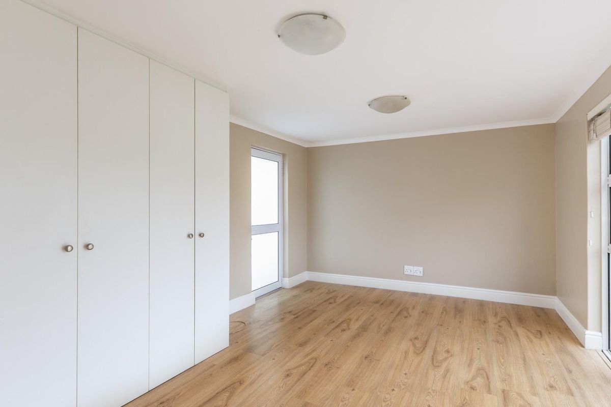 A bright, empty bedroom featuring light wood-look flooring, built-in white cabinetry, and large windows providing natural light.
