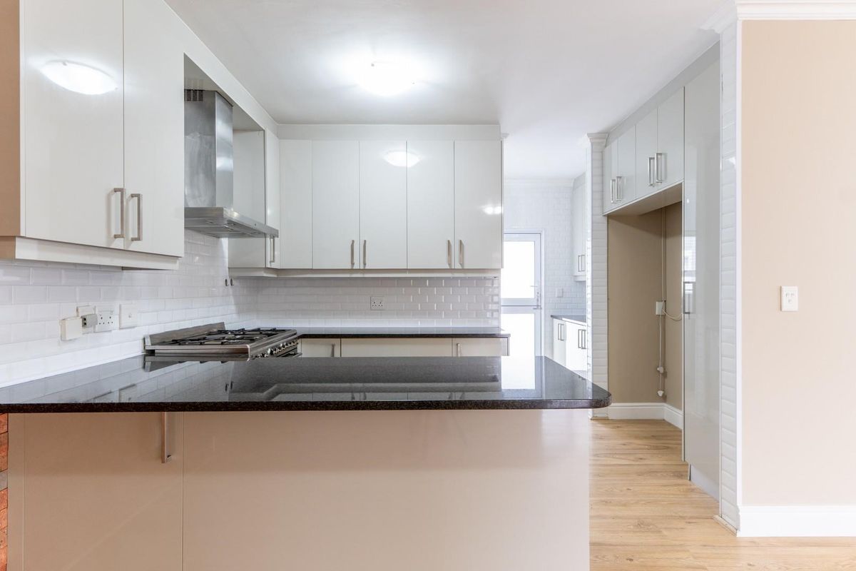 Modern kitchen featuring high-gloss cabinetry, dark granite countertops, a gas hob with stainless steel extractor, and subway tile backsplash, leading to a scullery area.