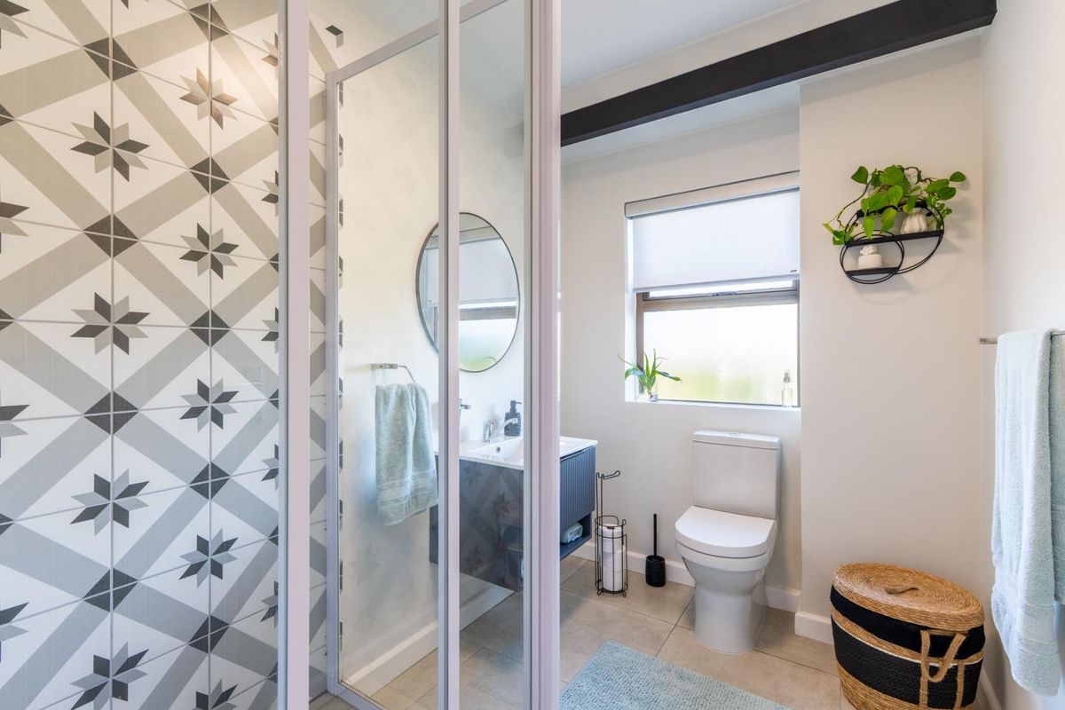 Modern bathroom featuring a glass-enclosed shower with patterned wall tiles, a vanity unit, and a toilet.