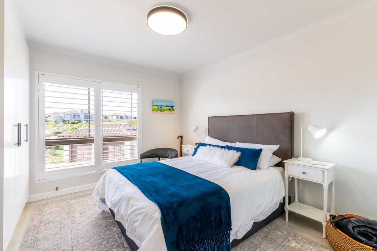 A bright and well-maintained bedroom featuring built-in cupboards, plantation shutters, and a modern ceiling light fixture.
