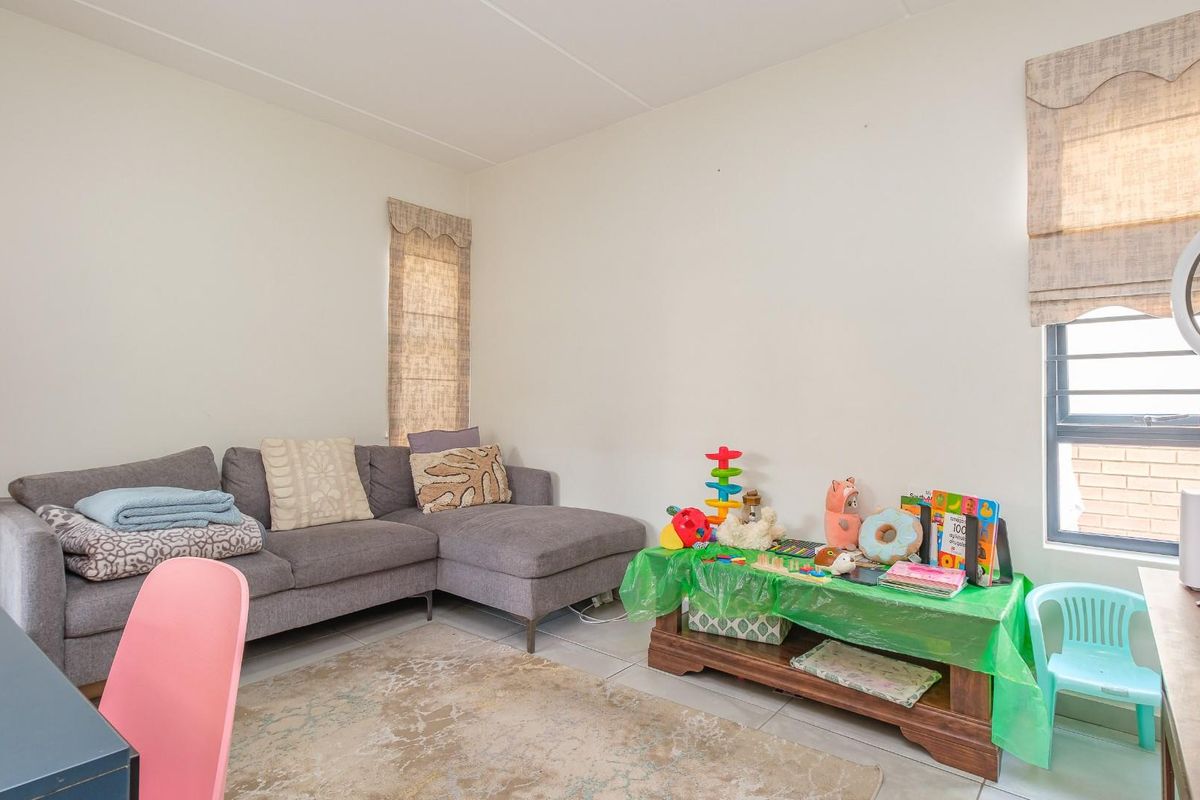 A functional living room featuring tiled flooring and large windows with fitted blinds, providing a bright and versatile space for relaxation.