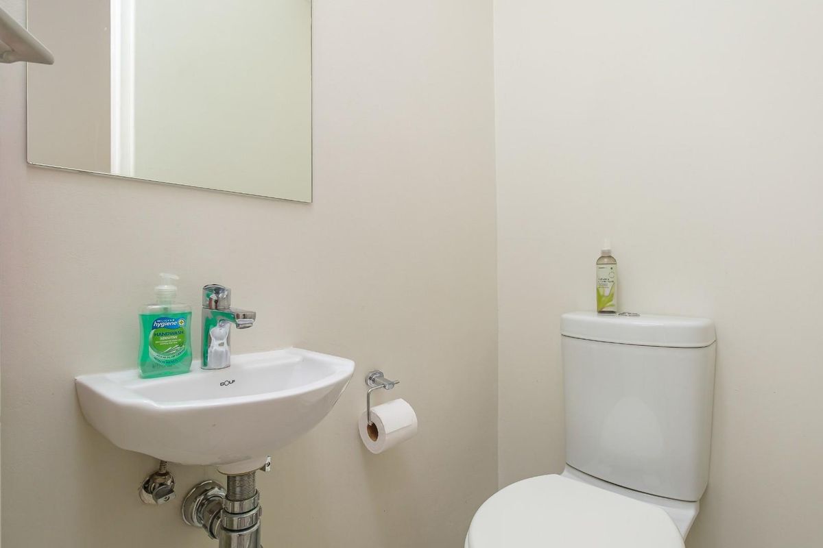 A compact guest bathroom featuring a wall-mounted basin with chrome mixer tap, a modern toilet, and a frameless mirror.