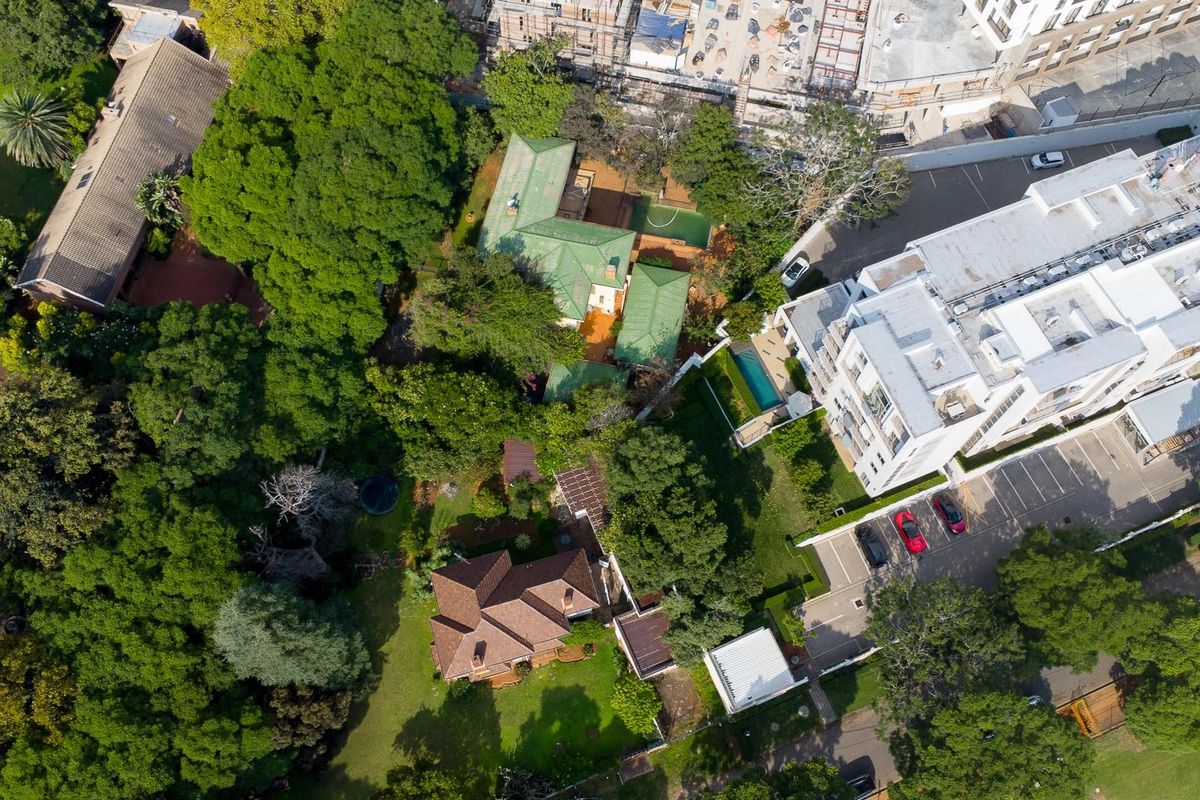 An aerial view of the residential property showcasing the main dwelling, surrounding mature trees, landscaped garden, and swimming pool area.