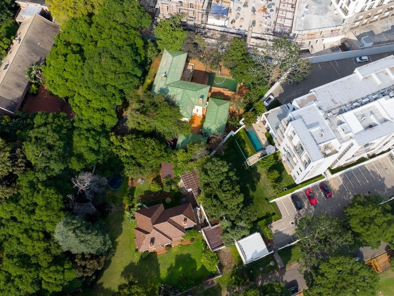 An aerial view of the residential property showcasing the main dwelling, surrounding mature trees, landscaped garden, and swimming pool area.