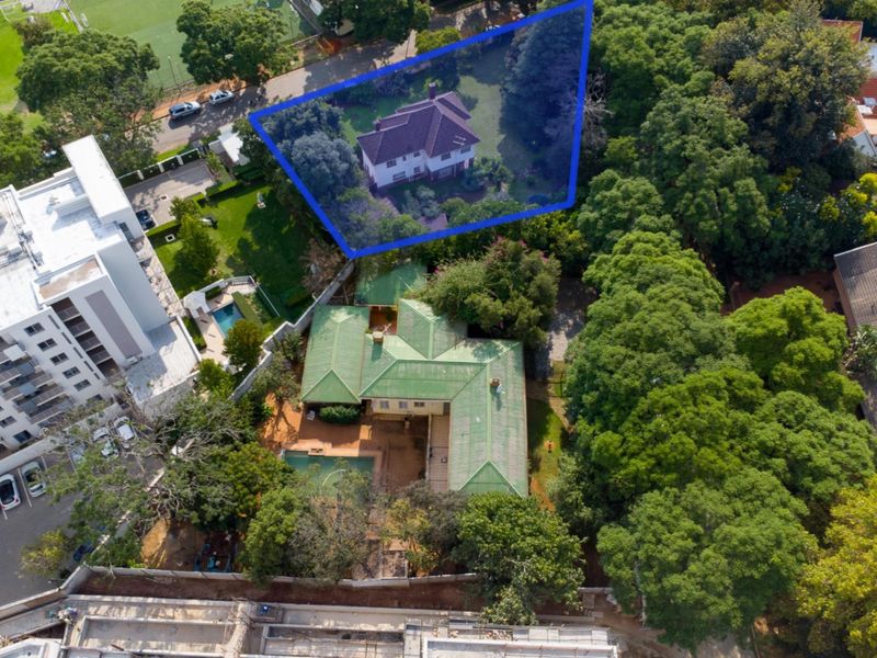 Aerial view of a residential property featuring a large house, swimming pool, and established garden with mature trees in a suburban setting.