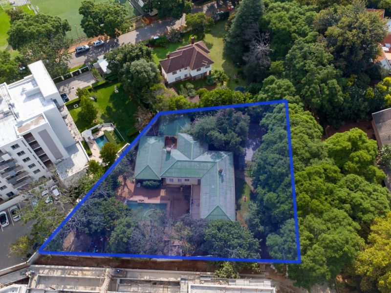 Aerial view of a residential property featuring a large garden, mature trees, a swimming pool, and a main dwelling with a pitched roof.