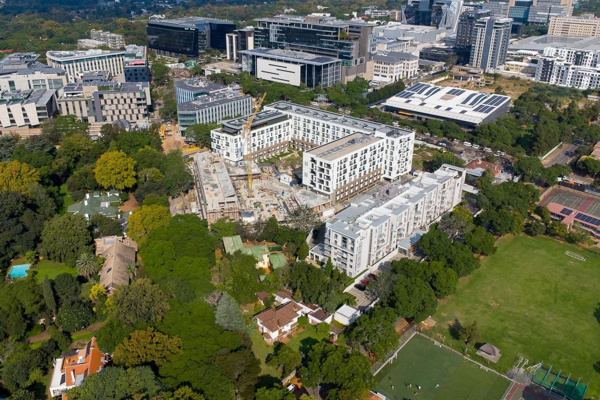 Aerial view of a residential development site situated within an established urban neighborhood with surrounding greenery and commercial buildings.