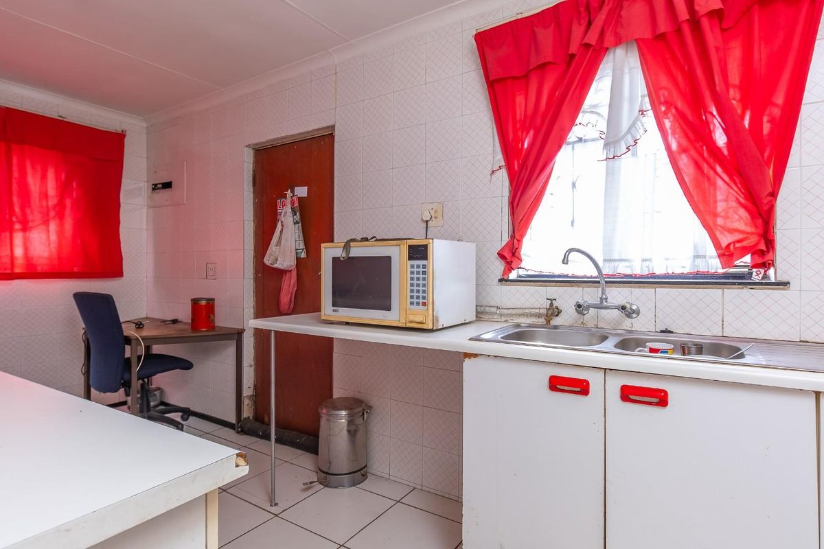A dated kitchen area featuring basic white cabinetry, a double basin sink, and tiled walls, offering a functional space with potential for modernization.