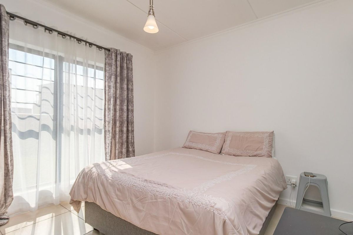 A bright and neutral bedroom featuring tiled flooring and a large sliding glass door that provides ample natural light.