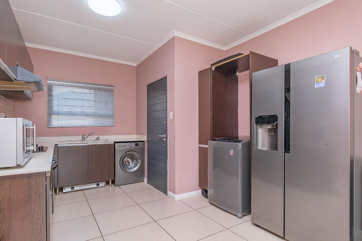 A functional kitchen featuring dark wood cabinetry, tiled flooring, a built-in extractor fan, and a dedicated space for laundry appliances.