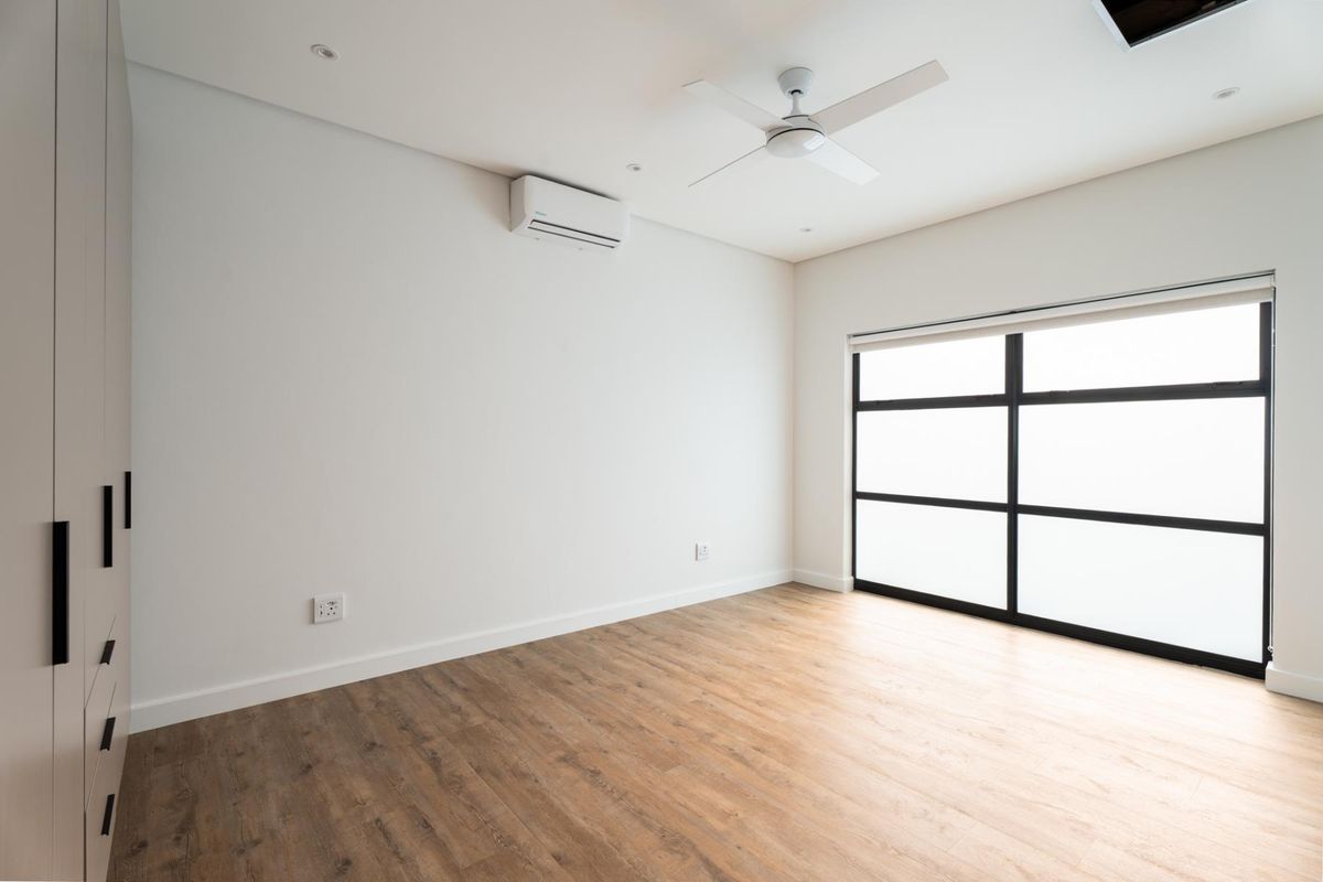 A bright, modern, and empty bedroom featuring laminate flooring, built-in cupboards, a ceiling fan, and a split-system air conditioner.