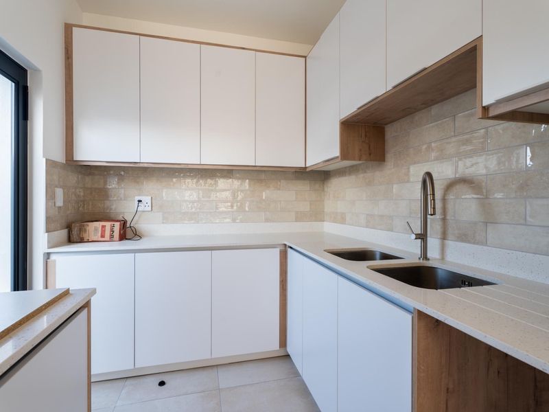 Modern kitchen featuring white cabinetry with wood accents, stone countertops, a double basin sink, and a stylish subway tile backsplash.