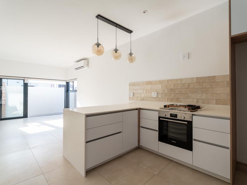 Modern open-plan kitchen featuring sleek cabinetry, stone countertops, subway tile backsplash, and built-in oven, flowing seamlessly into a bright living area with sliding doors.