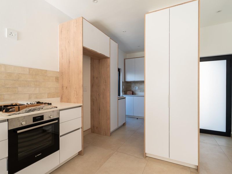 Modern kitchen featuring clean white cabinetry with wood-grain accents, built-in oven, hob, and neutral tiled flooring in a bright, contemporary space.