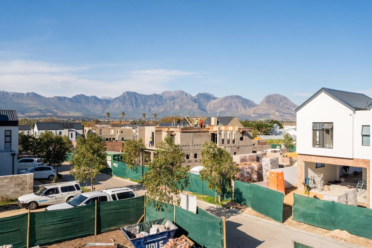 An elevated view of a residential construction site featuring ongoing building works, paved roads, and scenic mountain views in the background.