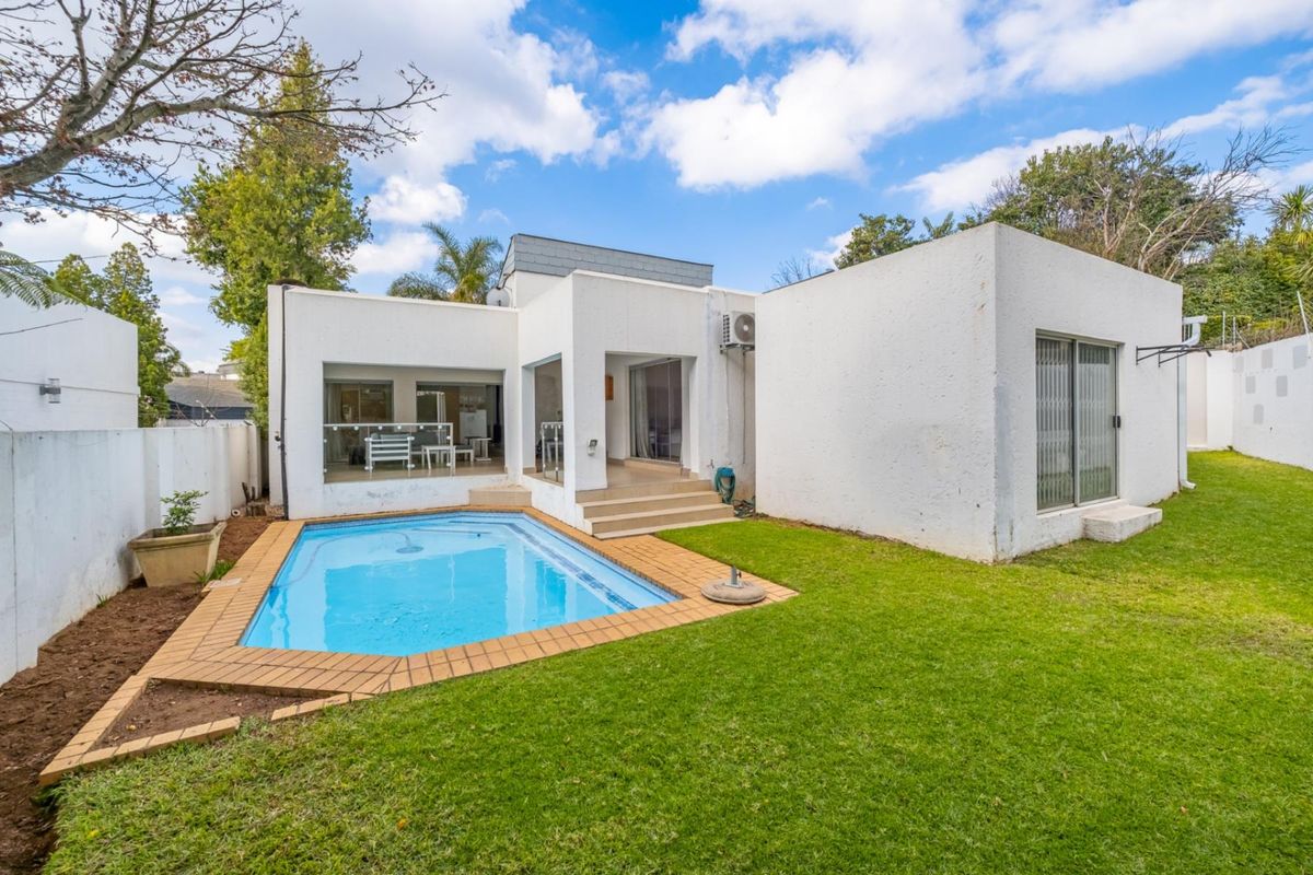 Rear view of the townhouse featuring a private swimming pool, paved patio area, and a well-maintained lawn with boundary walls.