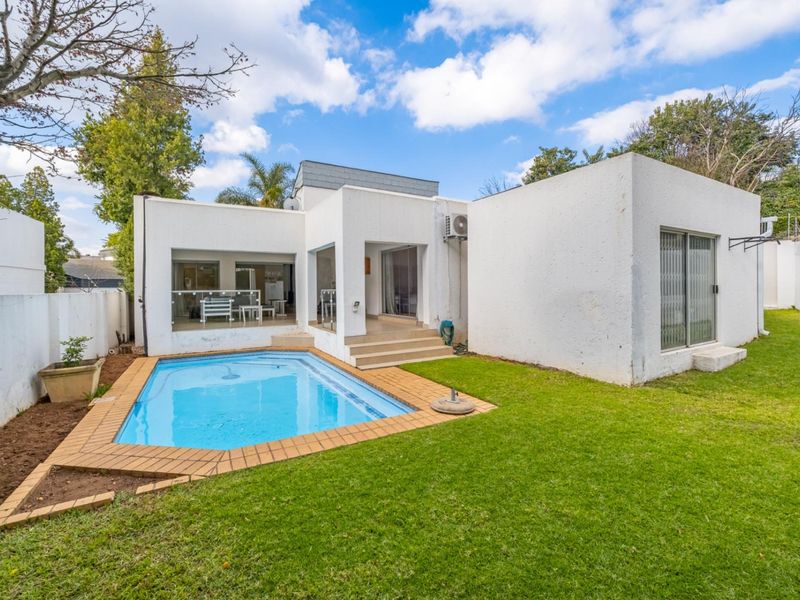 Rear view of the townhouse featuring a private swimming pool, paved patio area, and a well-maintained lawn with boundary walls.