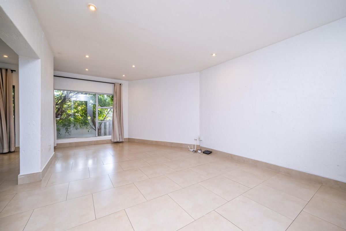 A bright and spacious empty living area featuring neutral tiled flooring, recessed downlighting, and a large window allowing for ample natural light.